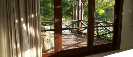 A room with a large sliding glass door leading to a wooden deck with a view of palm trees and a body of water.
