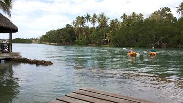Une rivière paisible, avec deux kayaks, une jetée en bois et une construction à toit de chaume.