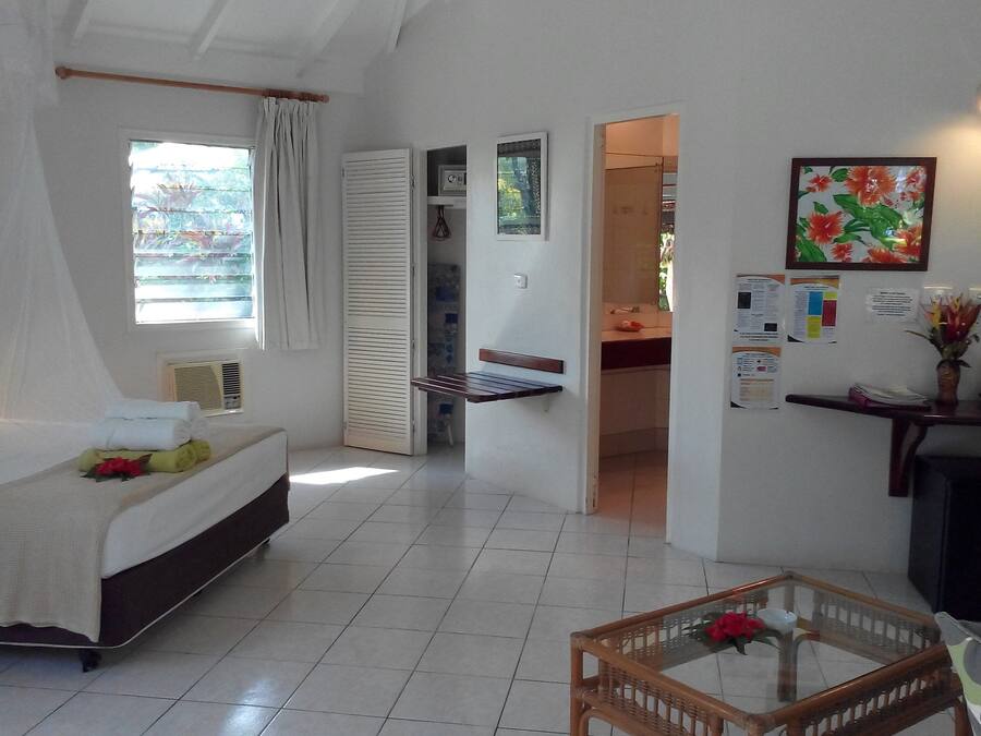 A bedroom with a bed, bedside table, and a window with curtains. There is a door leading to a bathroom.