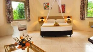 Ein Schlafzimmer mit Bett, Nachttischen, einem Sessel, einem Glastisch mit Blumen und Blick ins Grüne.