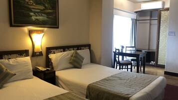 A hotel room with two beds, a desk, and a chair. There is a painting on the wall and a window with curtains.