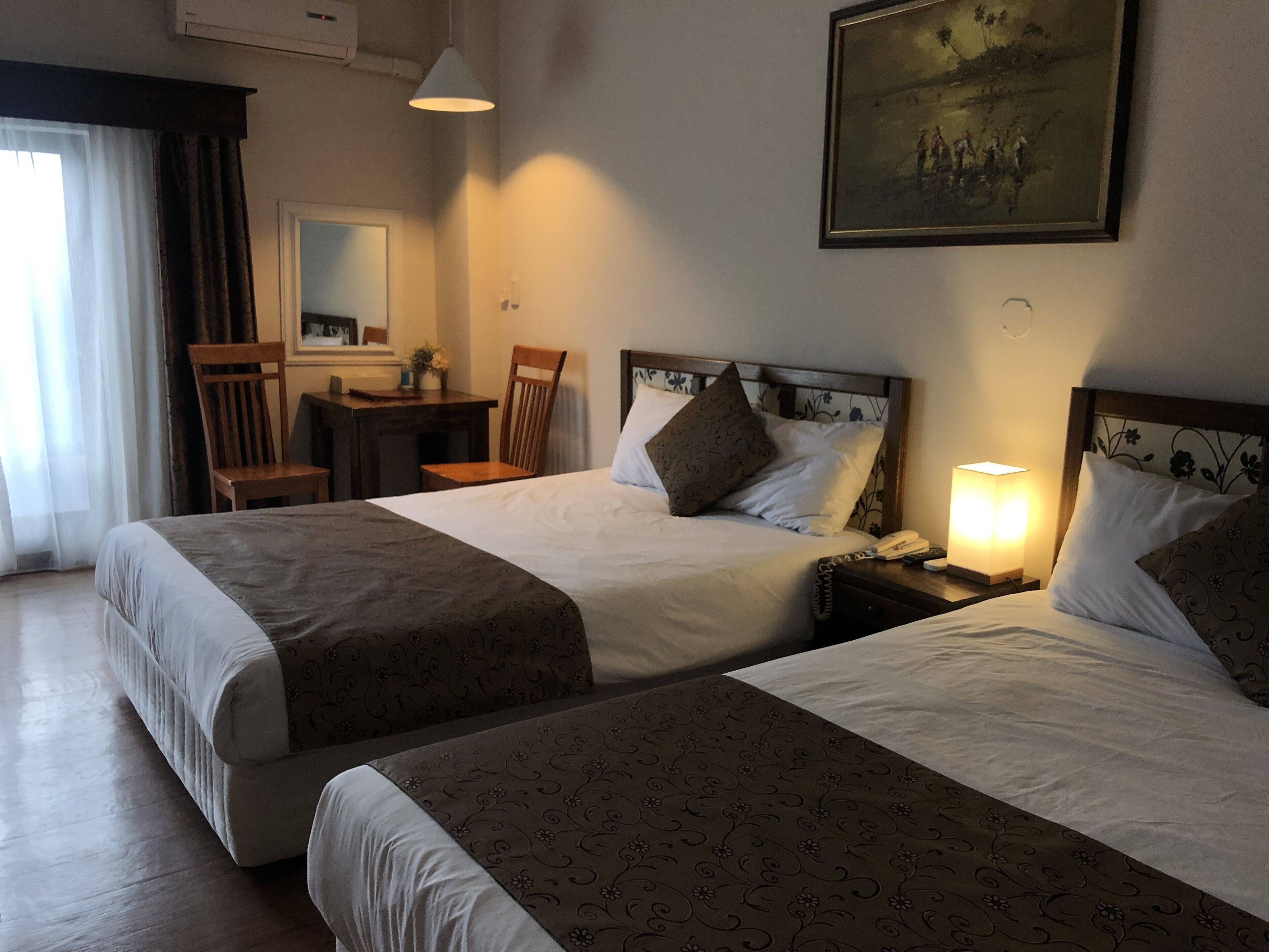 A hotel room with two beds, a desk, a chair, and a painting on the wall.