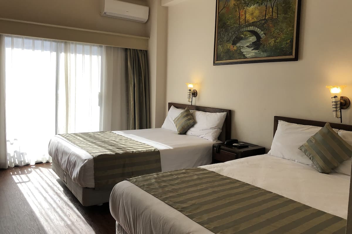 Quarto de hotel com duas camas, um quadro na parede e uma janela com cortinas.