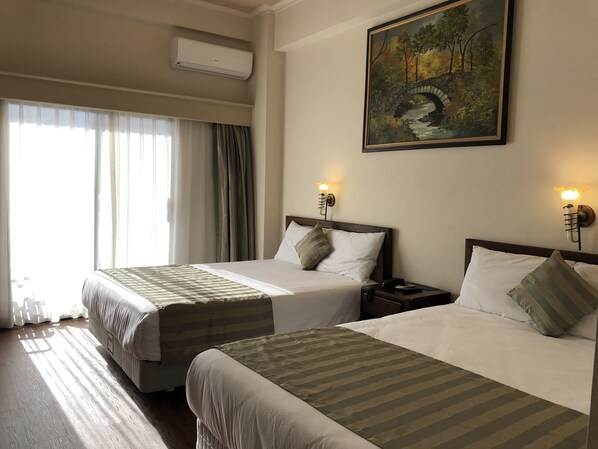 A hotel room with two beds, a painting on the wall, and a window with curtains.