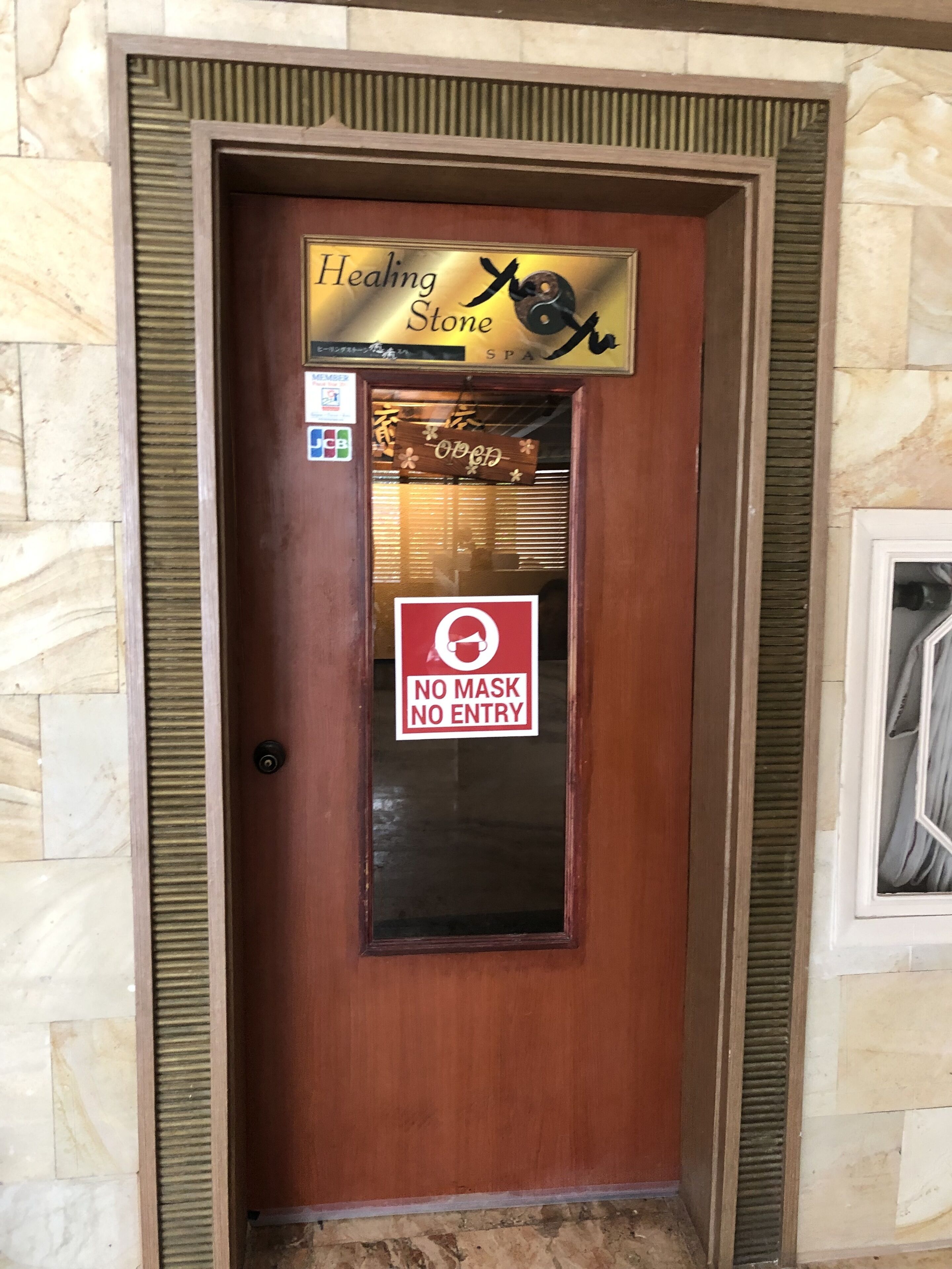 A wooden door with a sign reading "Healing Stone Spa" and a "No Mask No Entry" sign.