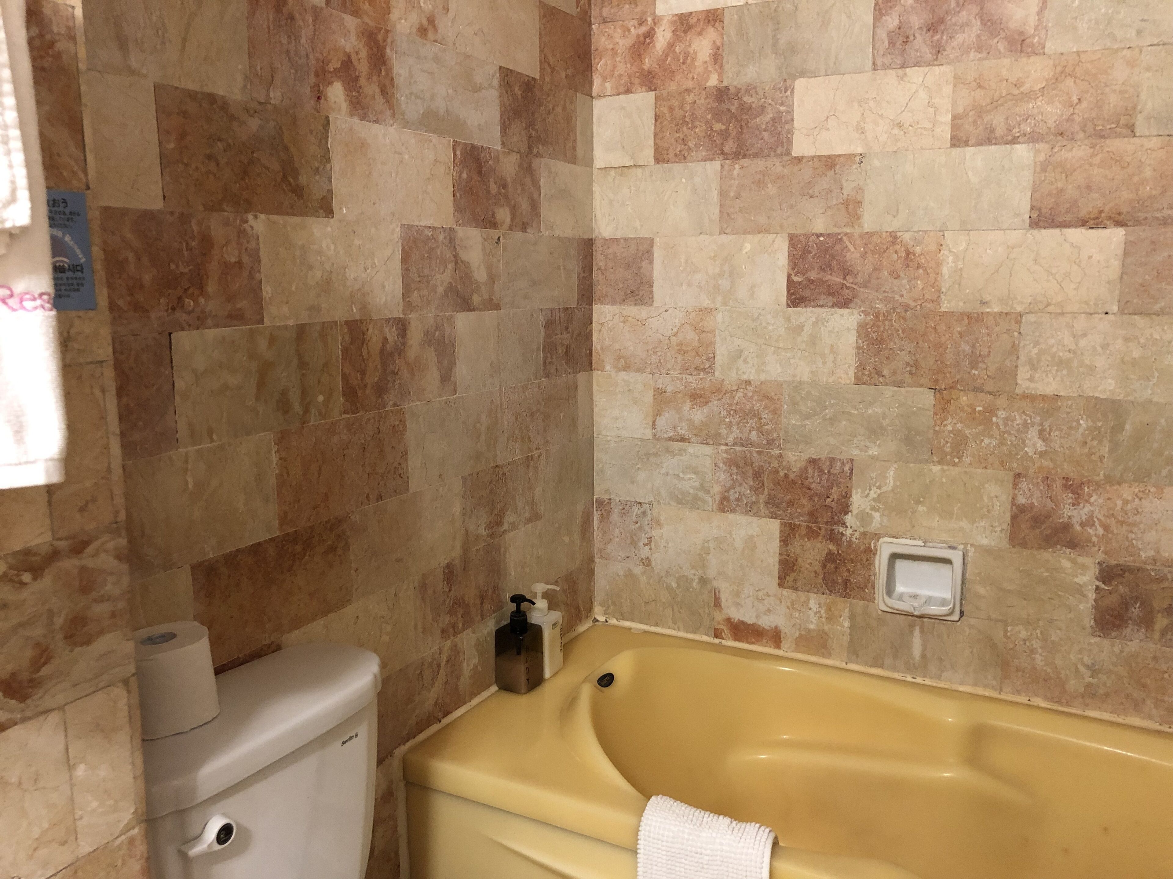A bathroom with a toilet, a yellow bathtub, and a tiled wall.