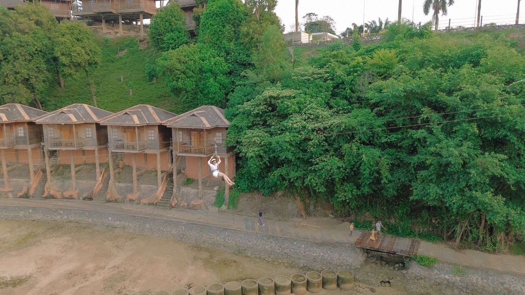 A traditional wooden house with a thatched roof, surrounded by lush greenery and a dirt path.