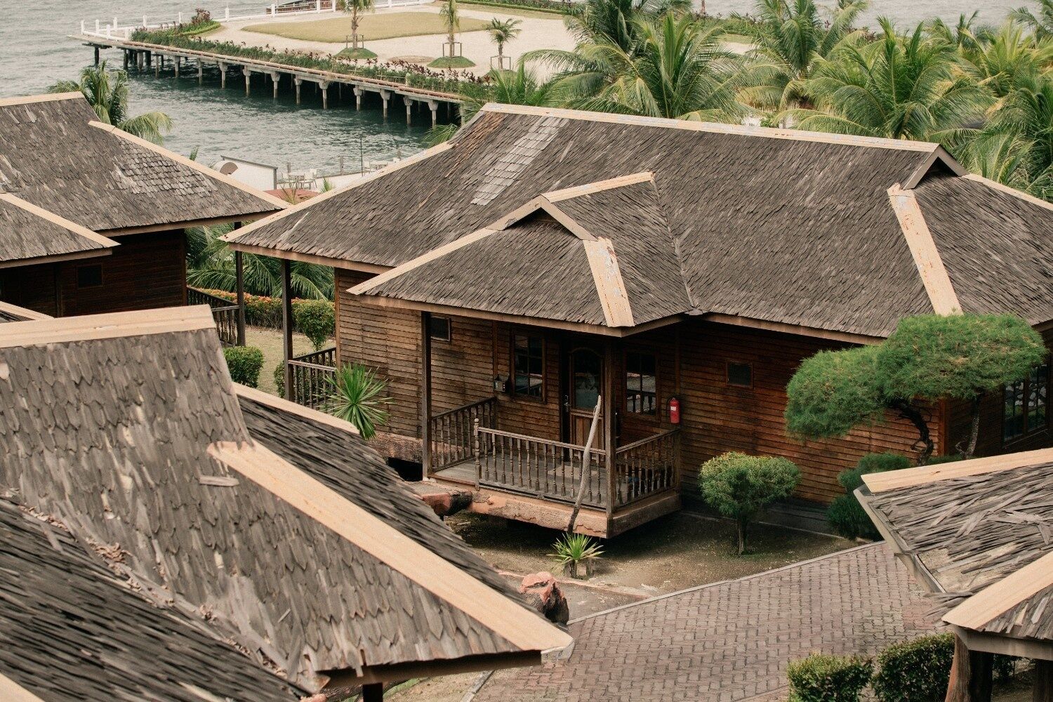 A row of wooden cabins with thatched roofs, a dock, and palm trees.