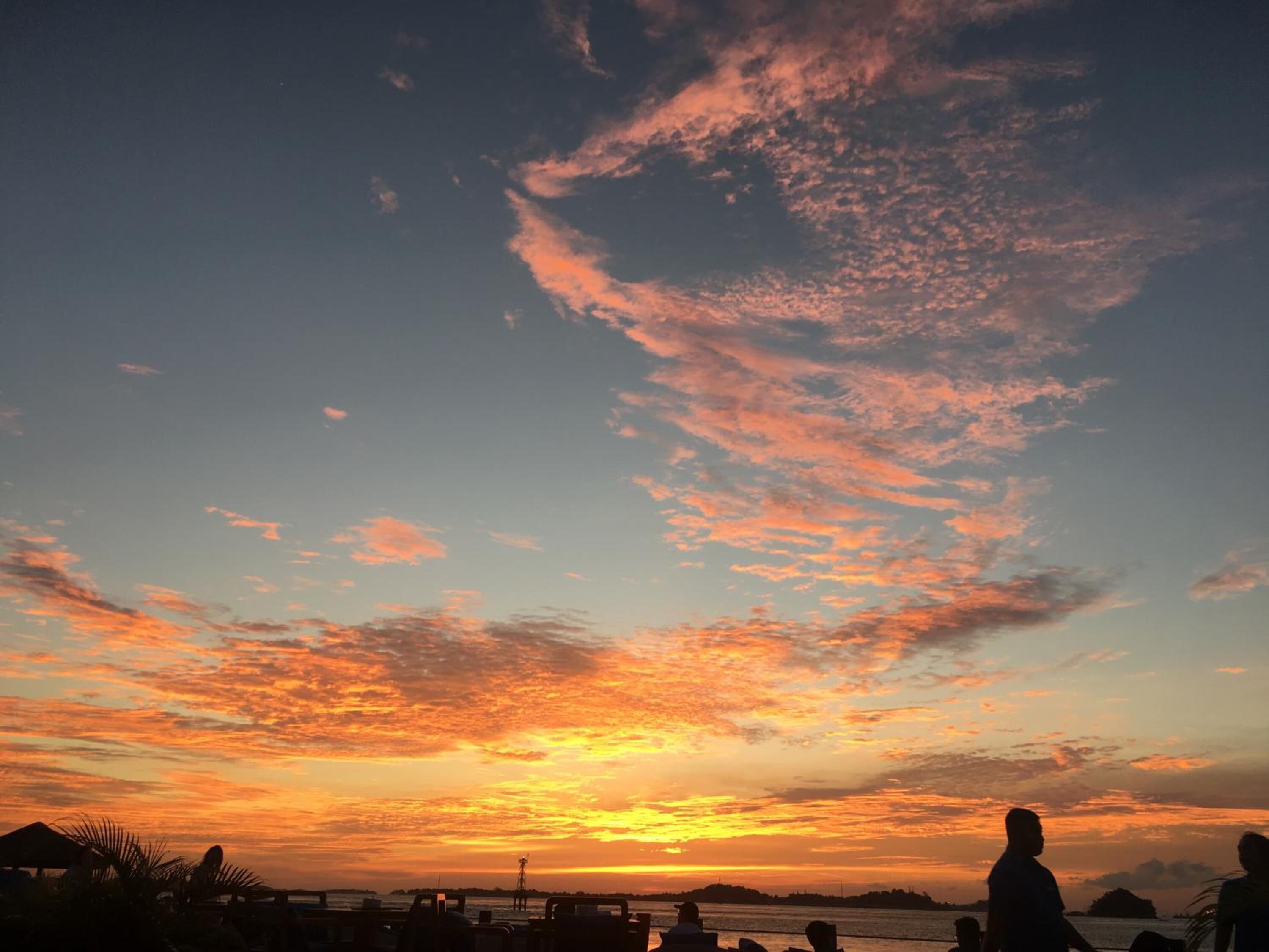 Ein Sonnenuntergang über dem Wasser, mit Silhouetten von Menschen und Palmen.