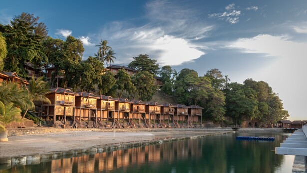 A waterfront hotel with multiple wooden buildings, a calm river, and lush greenery.