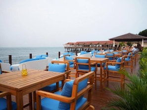 A seaside restaurant with wooden tables and blue cushioned chairs, overlooking the ocean.
