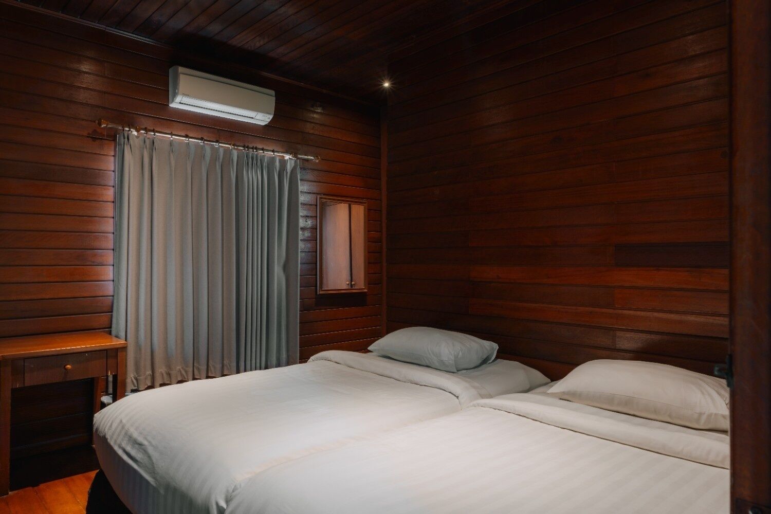 Una habitación con paneles de madera, una cama, un escritorio y un ventanal con cortinas.