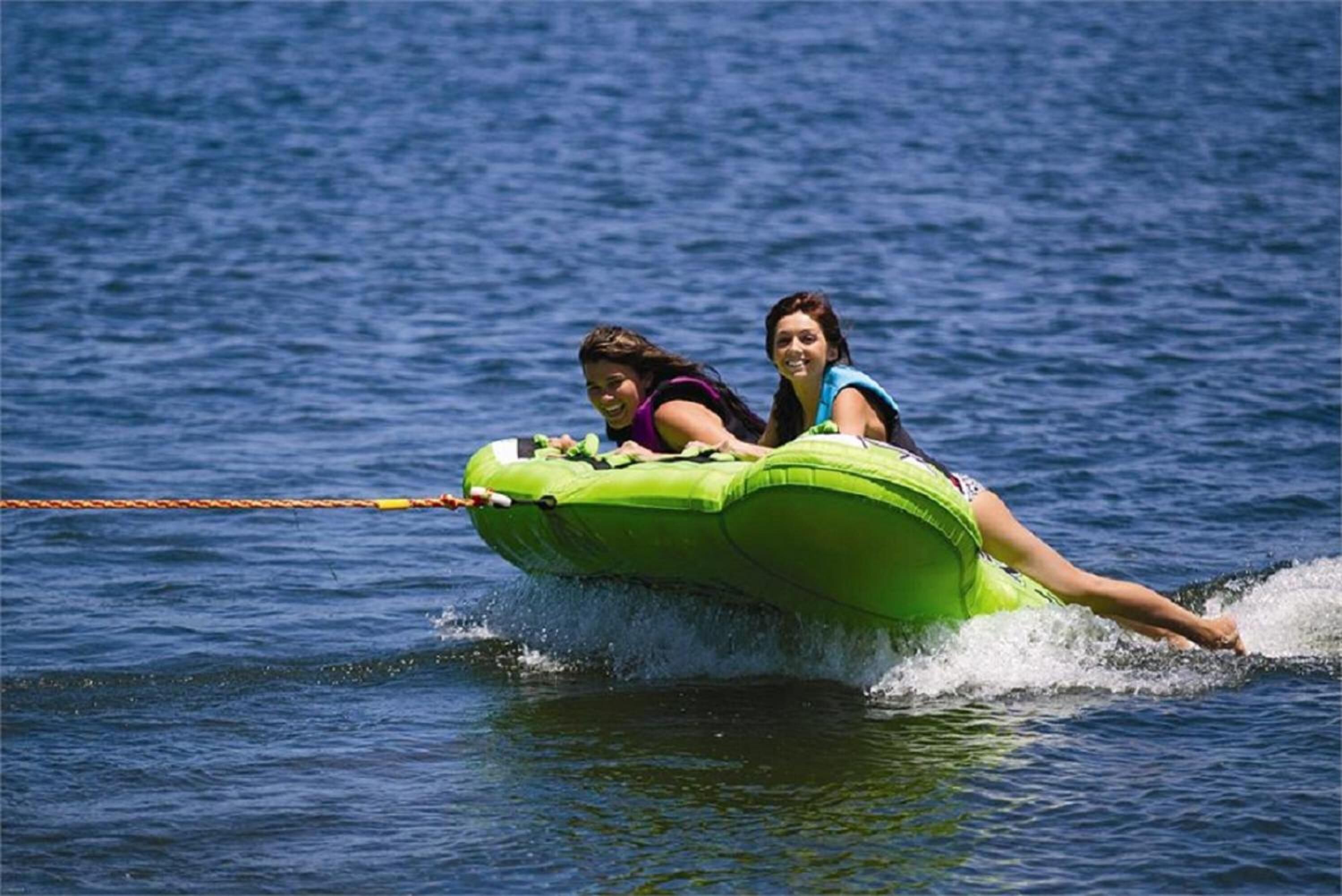 Two people on a green watercraft being towed by a rope.