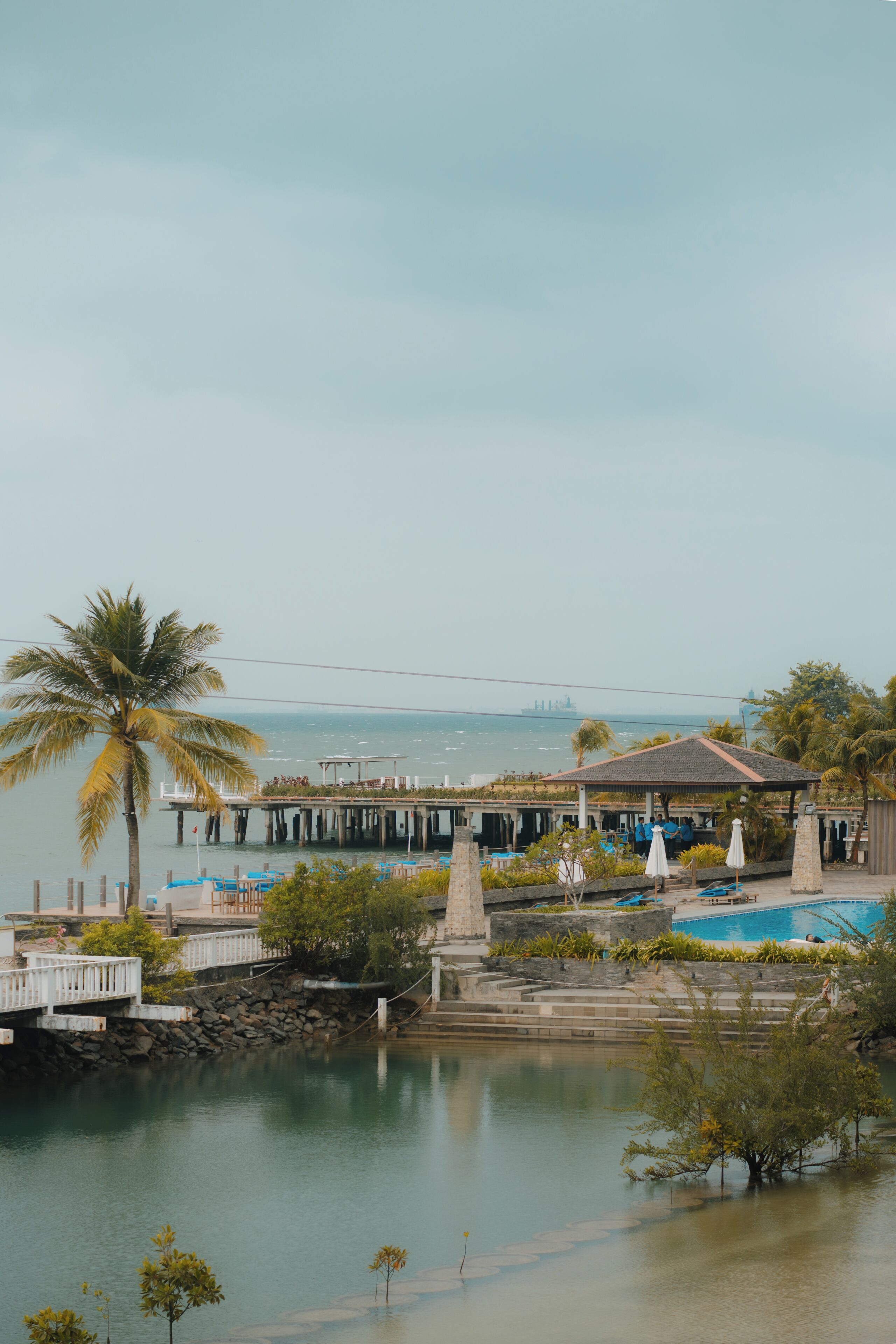 A waterfront resort with a pool, palm trees, and a pier.