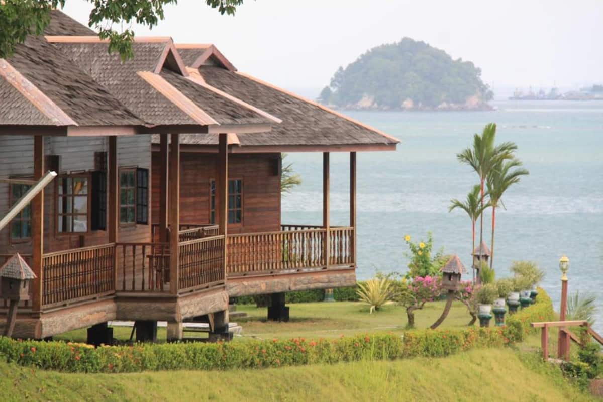 A wooden house with a balcony overlooking a body of water and a small island in the distance.