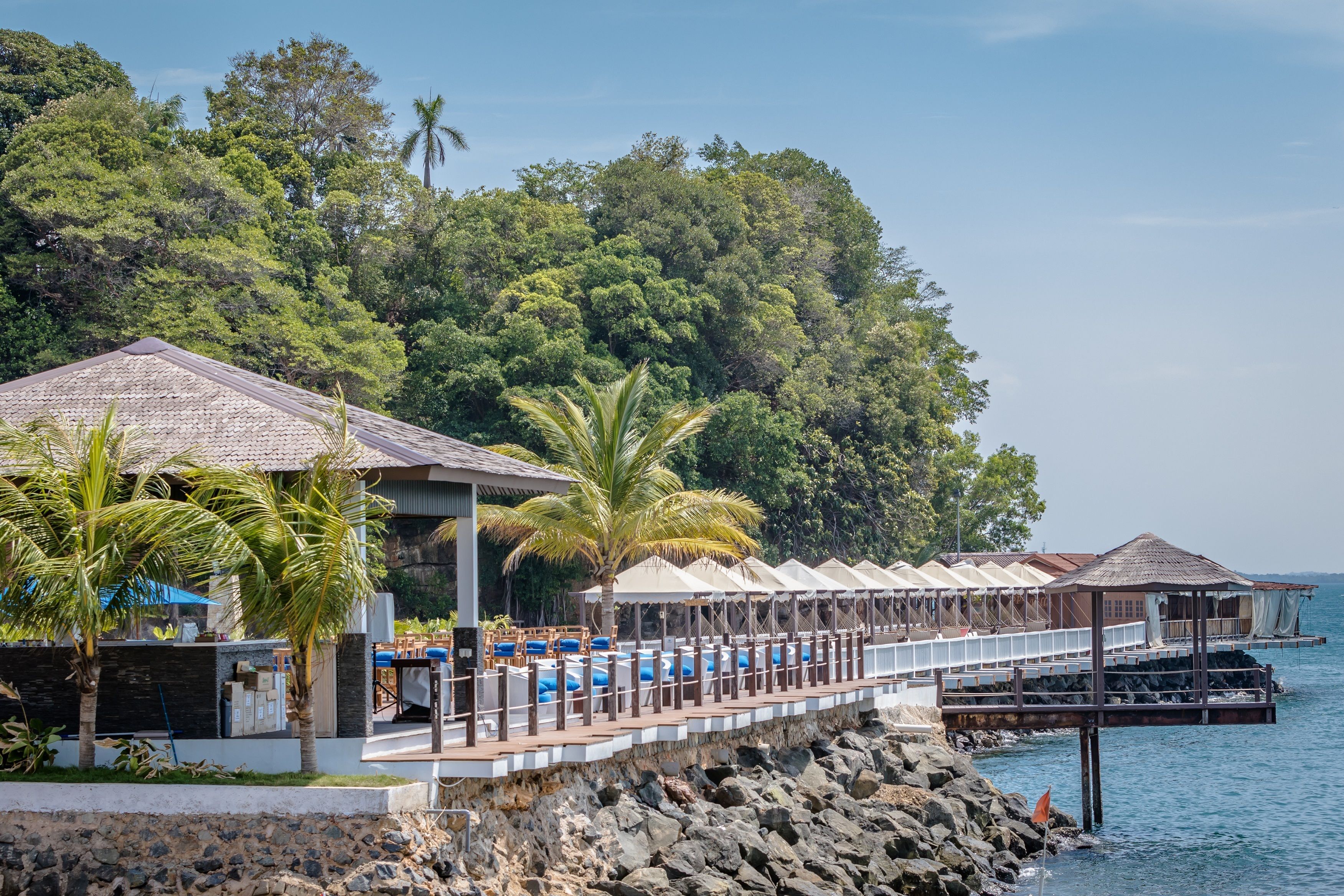 A seaside resort with a long pier, outdoor seating, and a pool area.