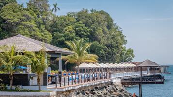 A seaside resort with a long pier, outdoor seating, and a pool area.