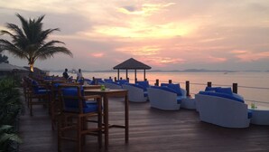 A deck with seating and a view of the sunset over the water.