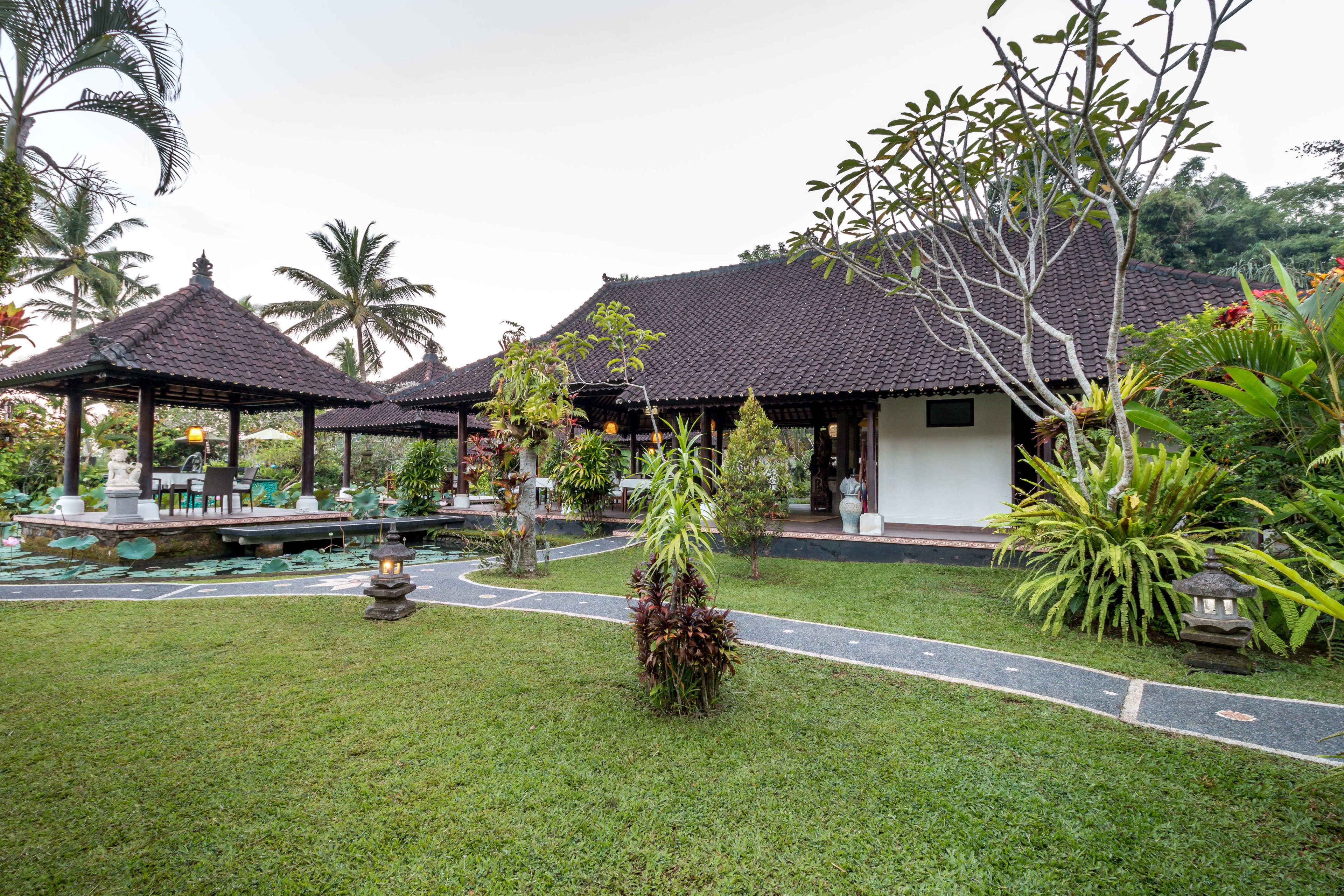 A traditional-style building with a tiled roof, surrounded by lush greenery and a small pond.