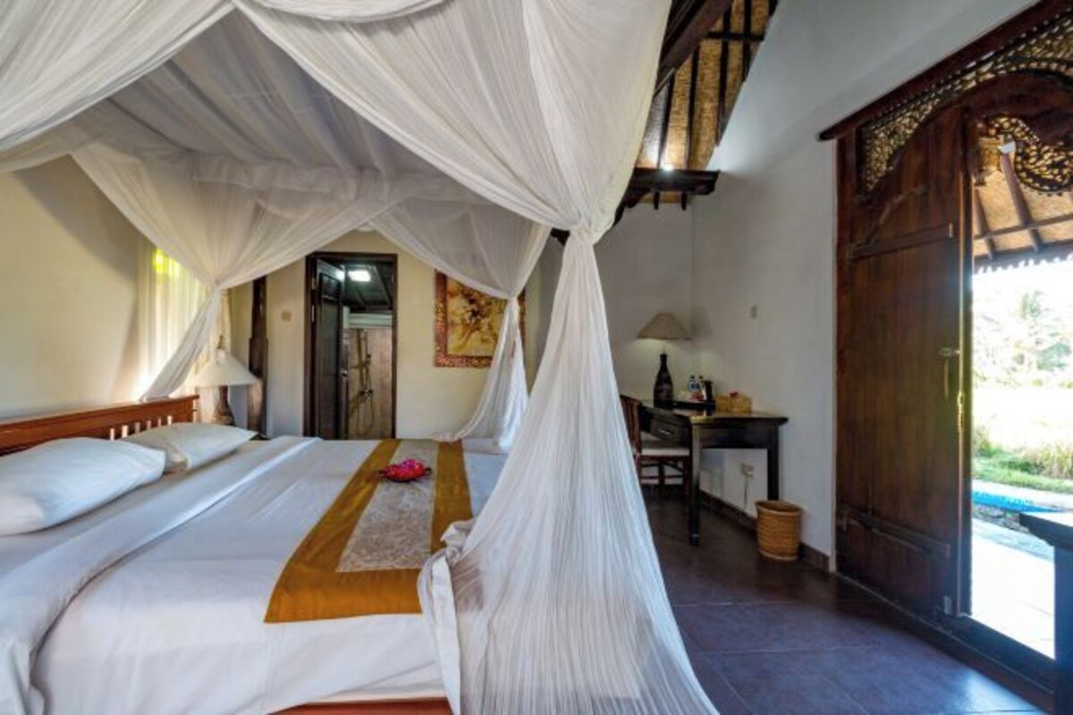 Una habitación con una cama bajo un dosel, un escritorio con una lámpara y vistas al exterior.
