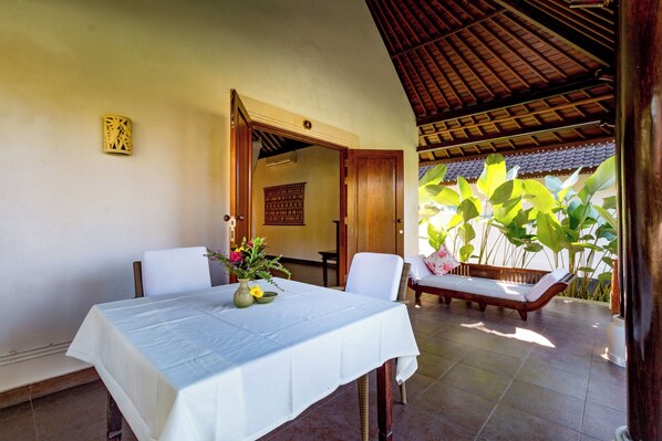 Un comedor con una mesa para dos, un banco y vistas a un jardín con plantas grandes.