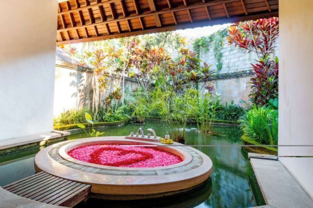 Un área de spa con un jacuzzi rodeado de exuberante follaje y un pequeño estanque.