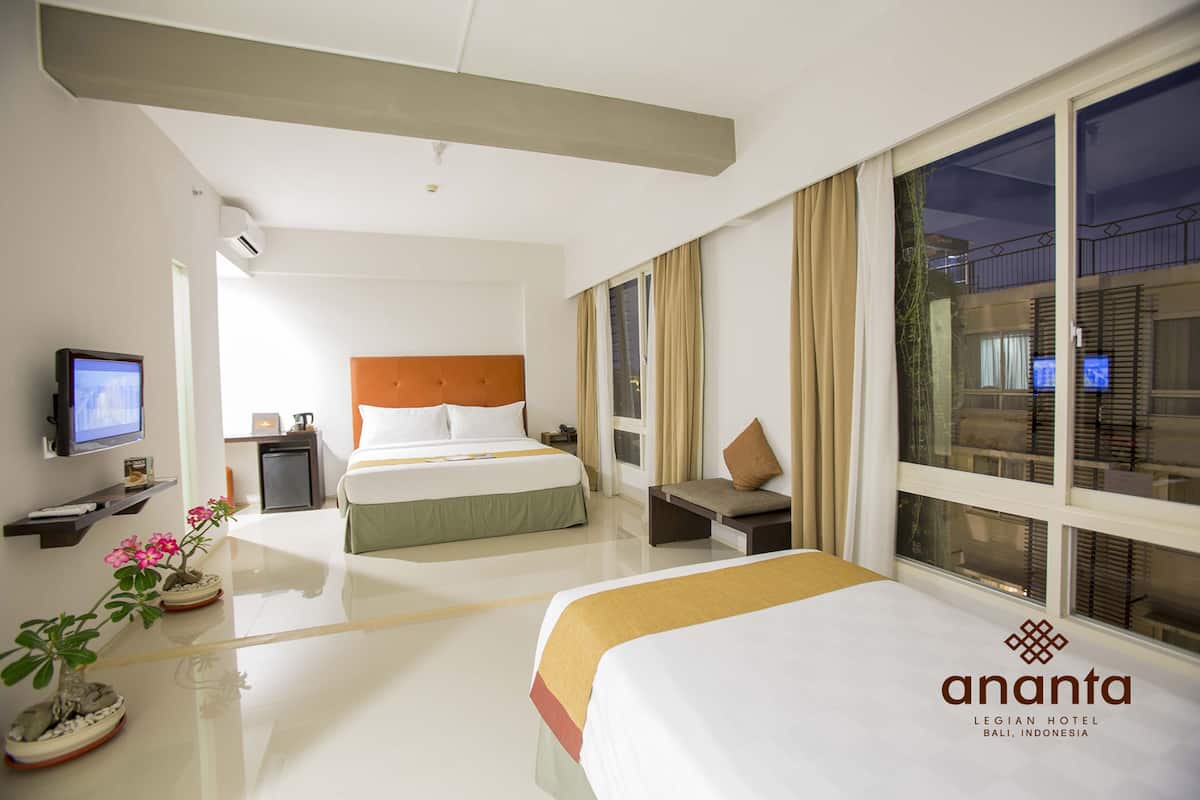 Quarto de hotel com duas camas, televisão, escrivaninha e janela com vista para a cidade.