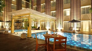 An indoor swimming pool with wooden deck seating and a covered area with umbrellas. - Ananta Legian Hotel (Legian)