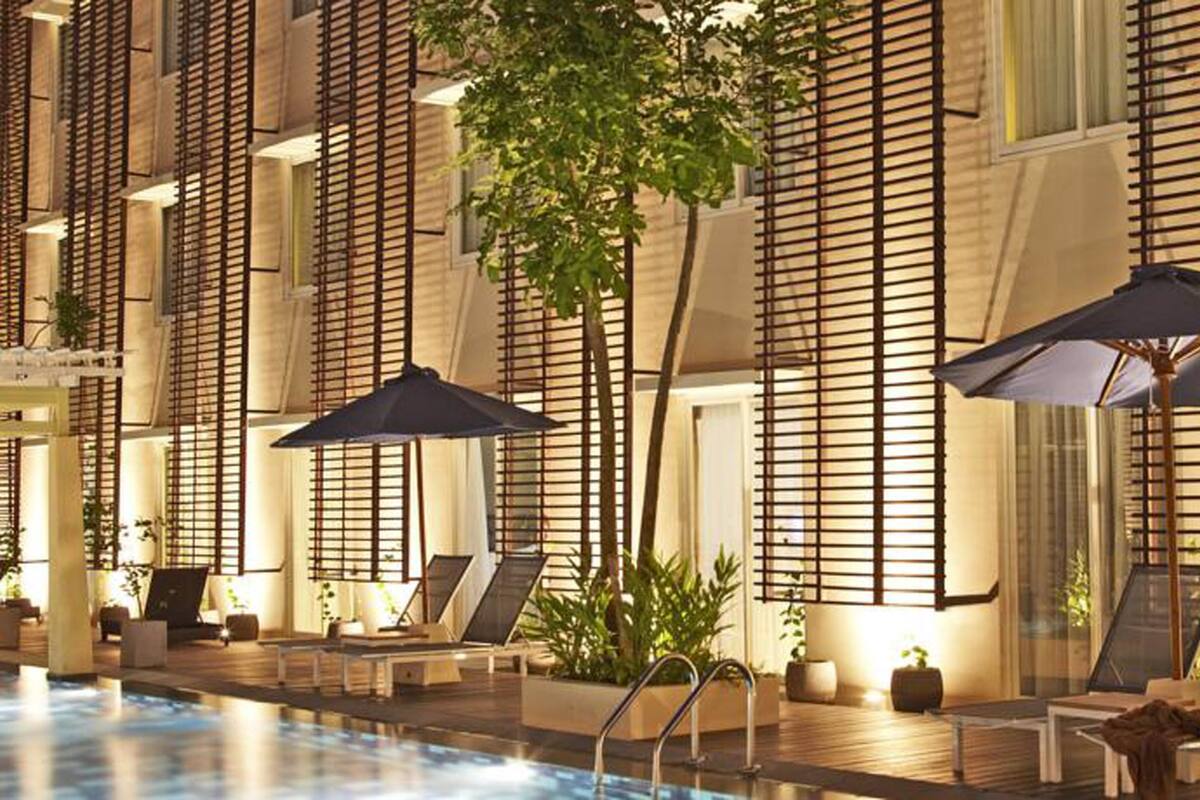 Área de piscina com espreguiçadeiras e guarda-sóis, cercada por ripas de madeira e plantas em vasos.