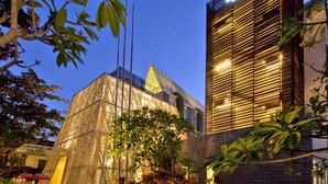 A hotel with a modern architectural design, featuring a prominent glass facade and a well-lit entrance area with plants and outdoor seating. - Ananta Legian Hotel (Legian)