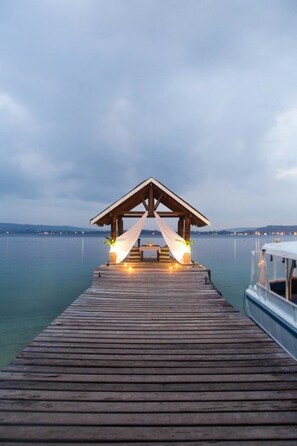 A wooden pier leading to a covered area with lights and a hammock.
