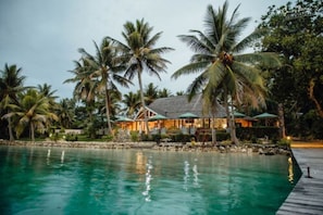 A resort with a swimming pool, palm trees, and a building with a thatched roof.