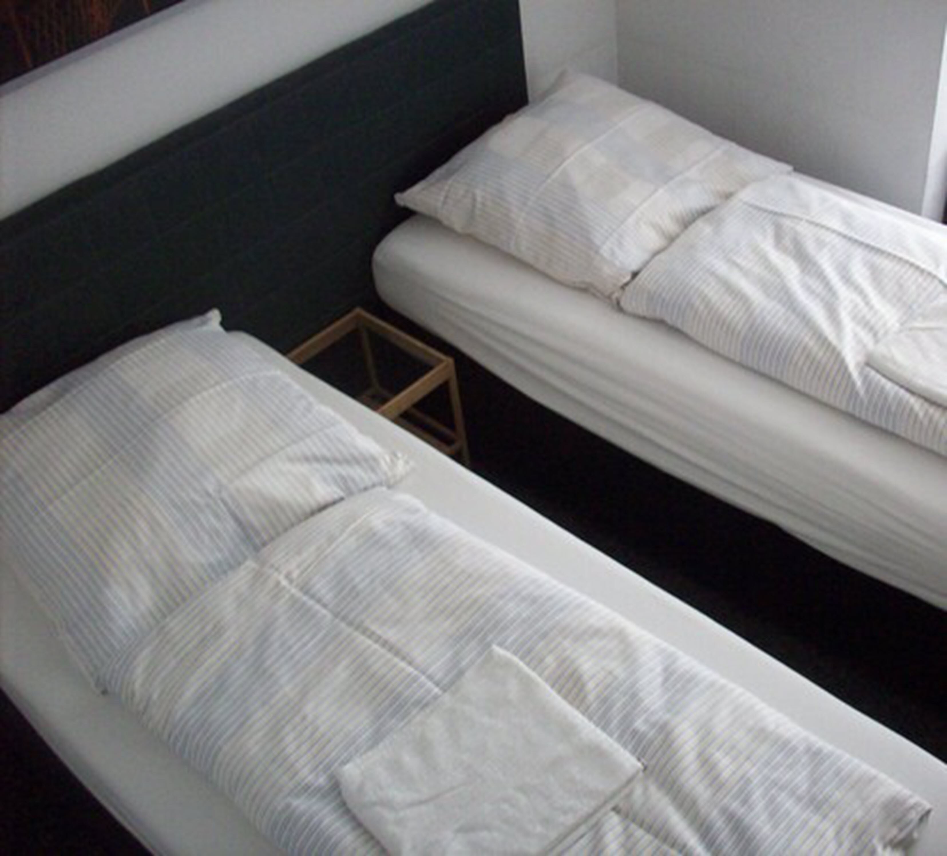 Una cama de matrimonio con dos plazas, con un cabecero oscuro y ropa de cama blanca.
