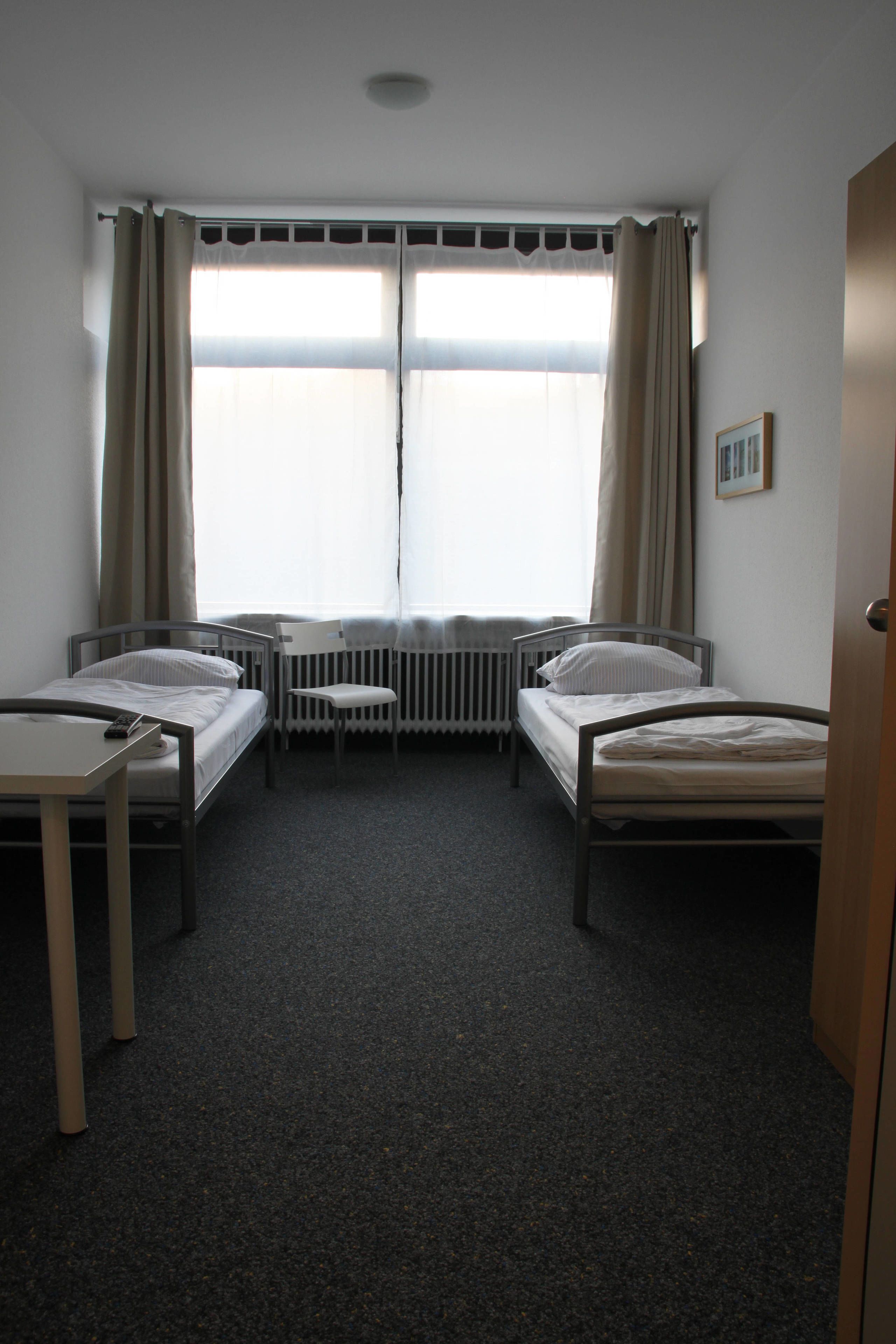A room with two single beds, a small table, and a chair.
