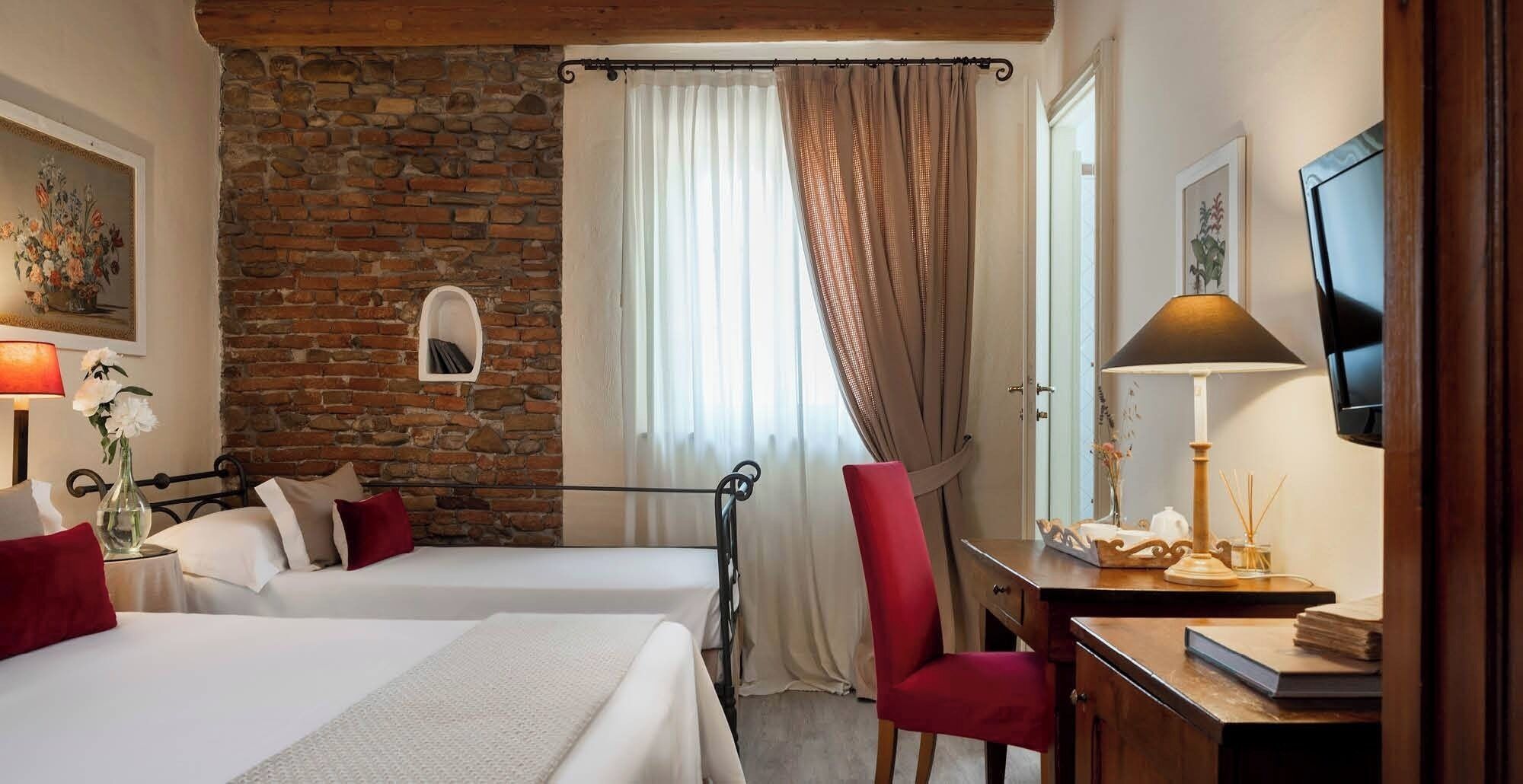 Una habitación con dos camas, un escritorio, una silla, un televisor y una pared de piedra.