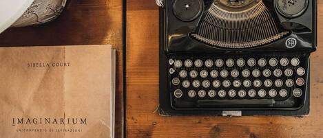 A vintage typewriter on a wooden surface with a brown paper bag labeled "Sibella Court" and a book titled "IMAGINARIUM UN COMPENDIO DI ISPIAZIONI".