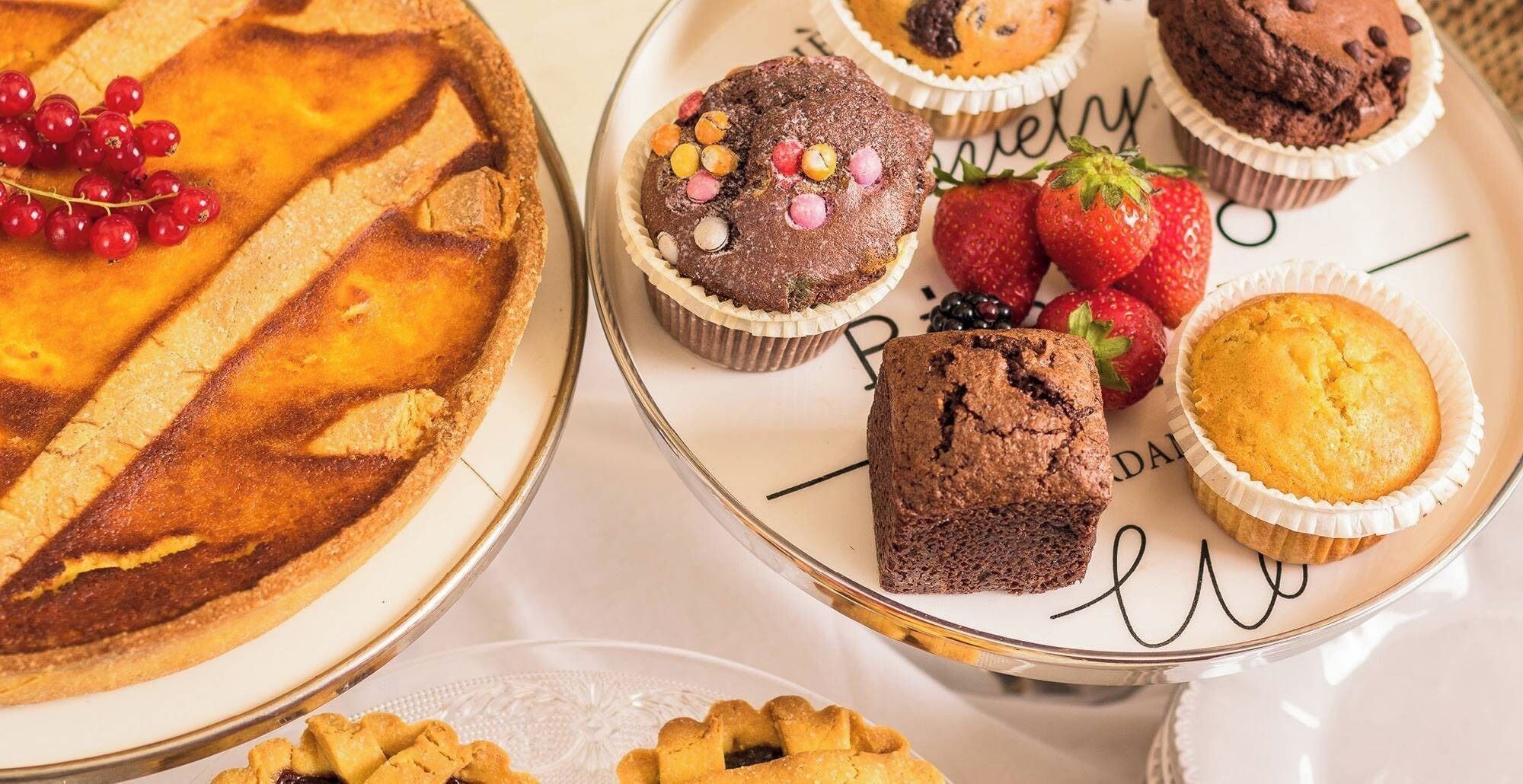 Varietat de productes de forneria, com ara una tartaleta, muffins i una tarta, disposats sobre un plat blanc amb text decoratiu.