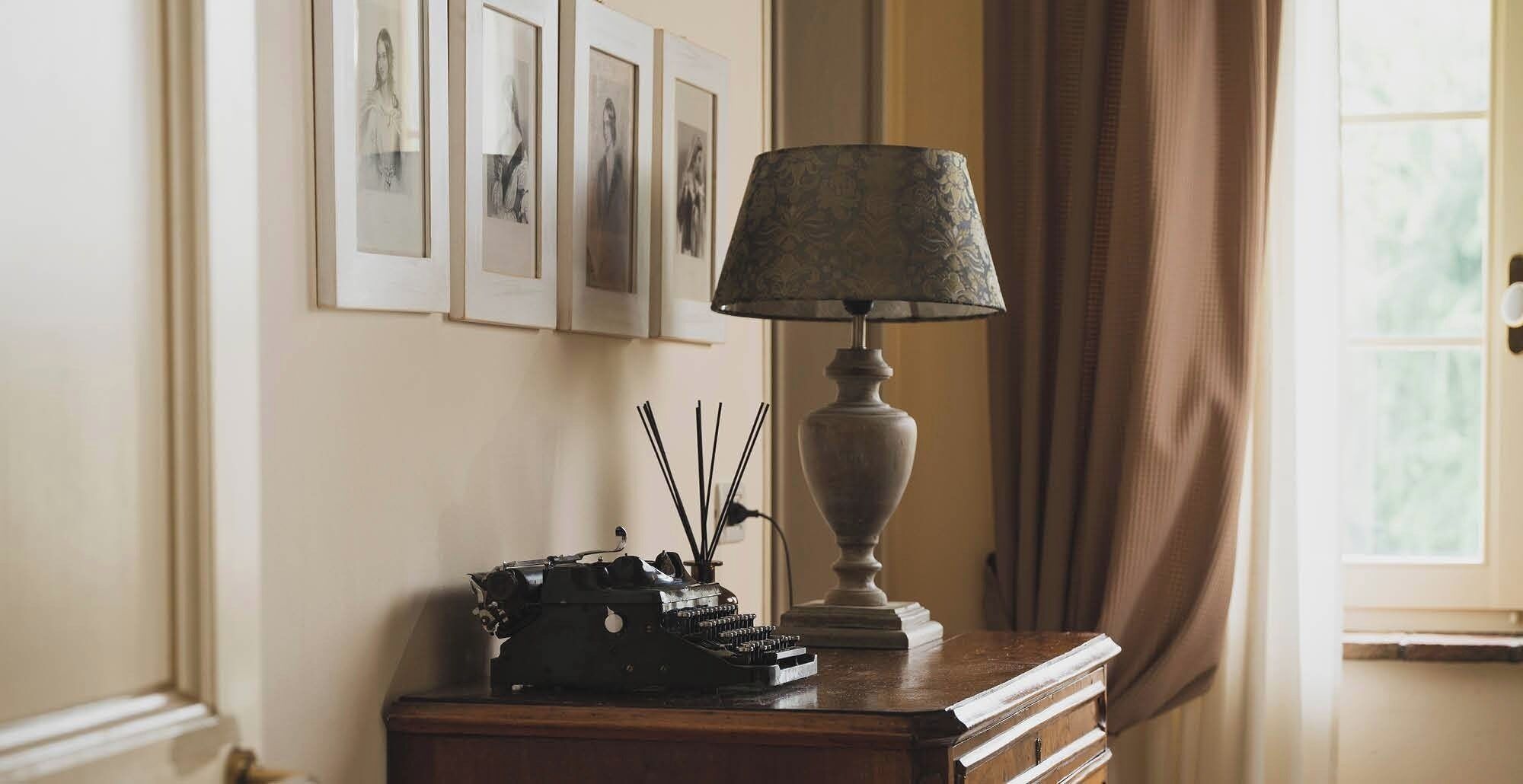 A desk with a lamp, a typewriter, and framed pictures on the wall.