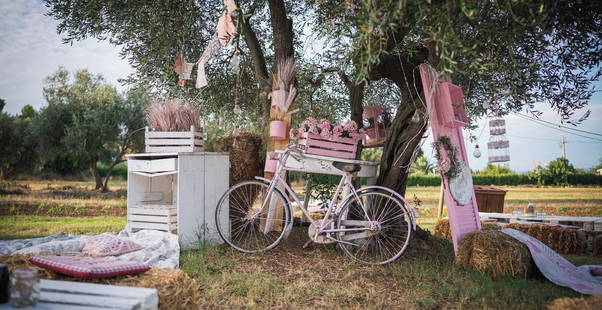 Un entorno rústico al aire libre con una bicicleta antigua, cajas de madera y un asiento de bicicleta rosa.
