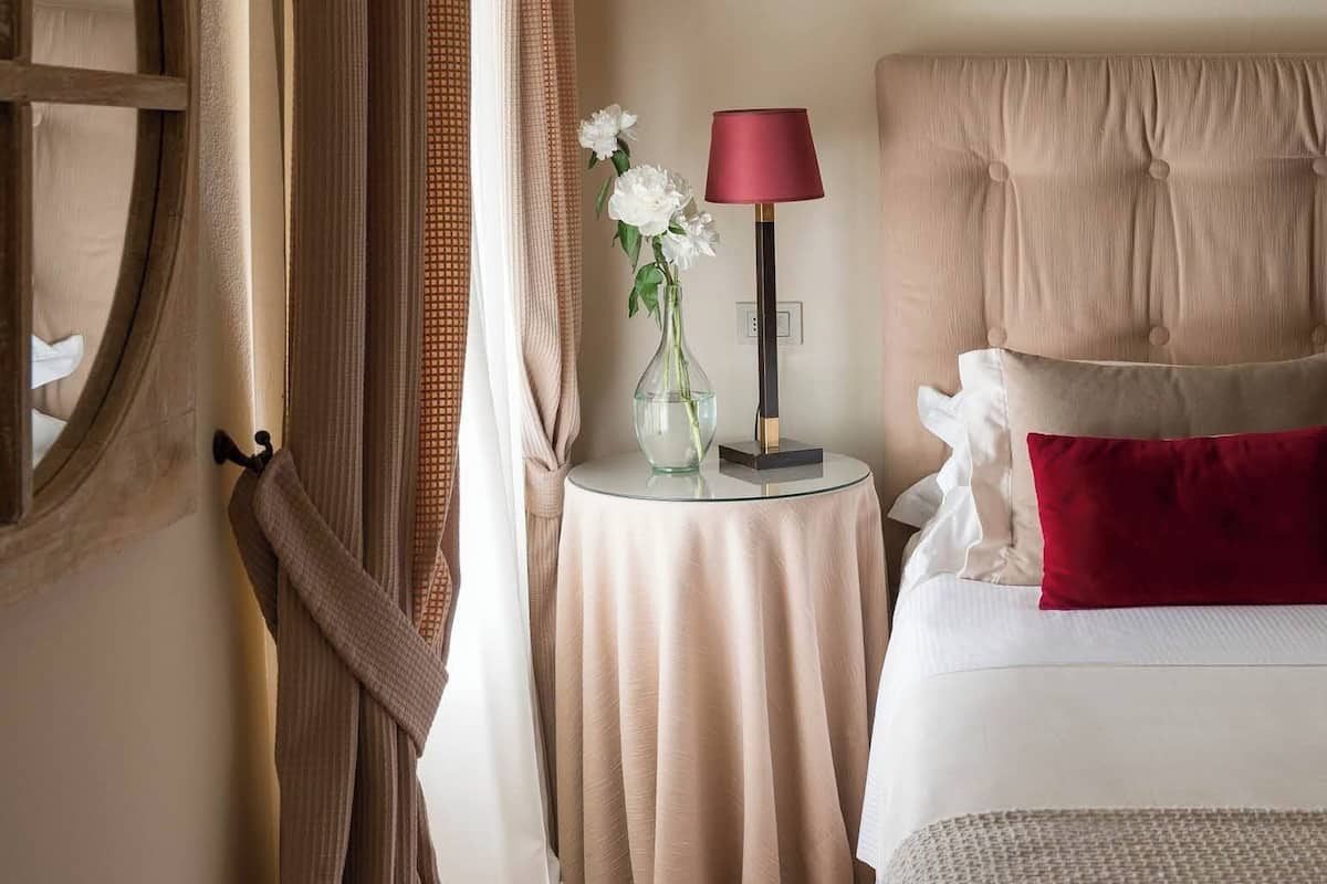 A hotel room with a large bed, a bedside table with a lamp, and a vase of flowers.