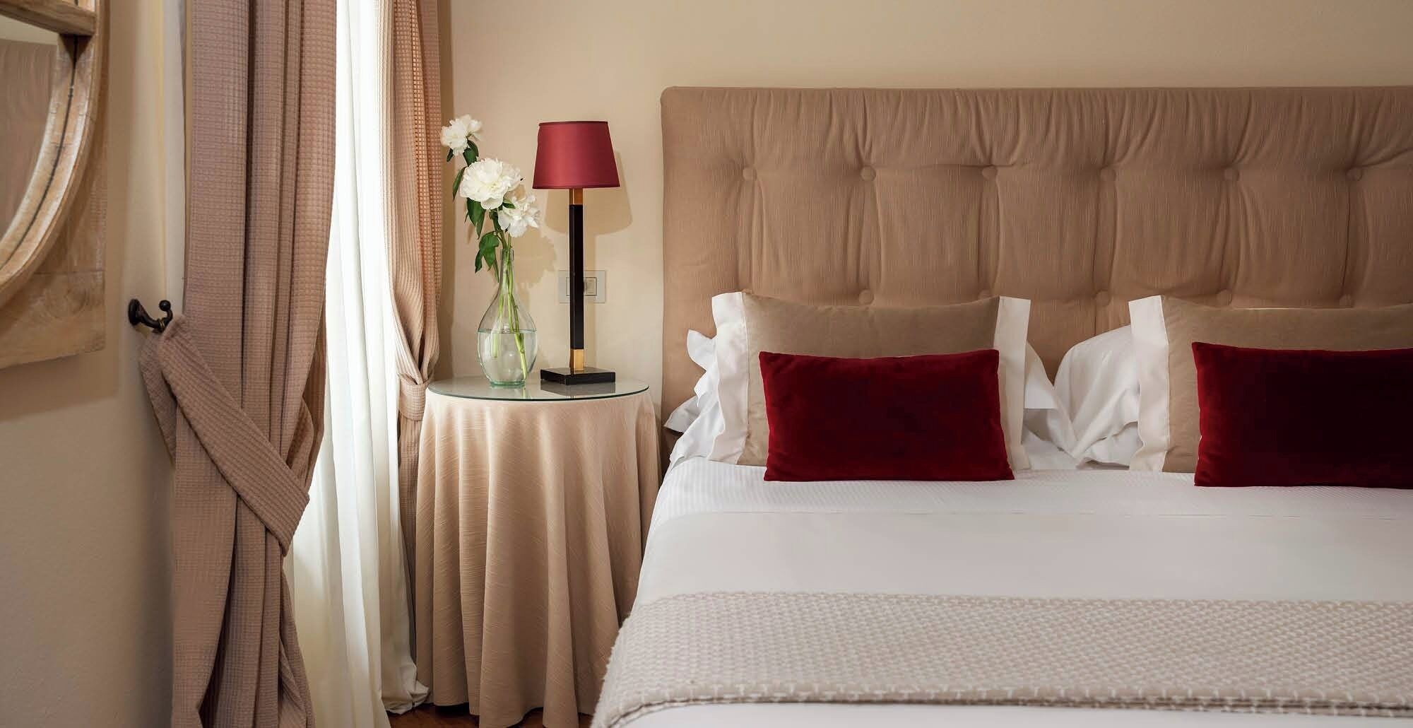 Quarto de hotel com uma cama grande, mesa de cabeceira com abajur e um vaso com flores.