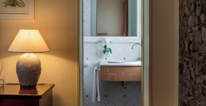 Ein Badezimmer mit einem weißen Waschbecken, einem Spiegel, einer hängenden Pflanze und einer Lampe auf einem Holztischchen.
