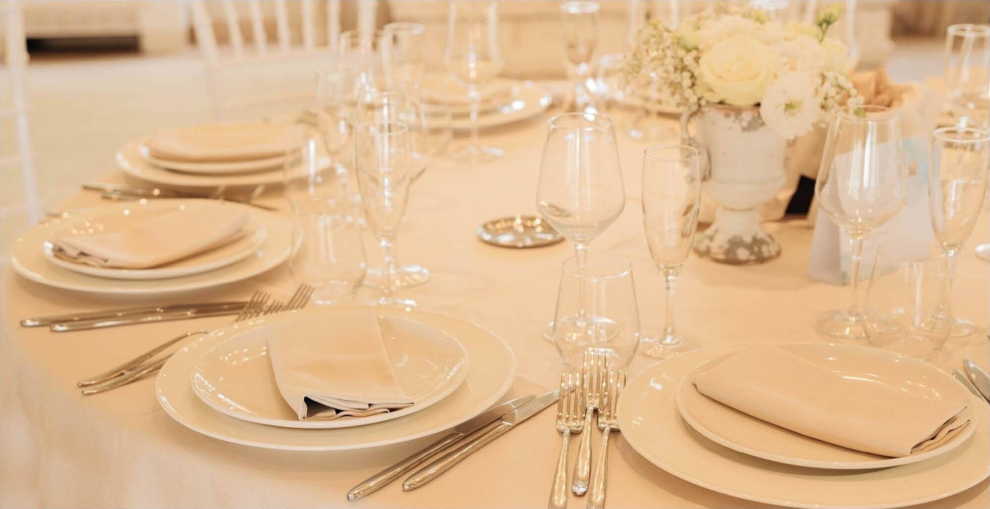Une table dressée pour un événement formel, avec plusieurs assiettes, couverts et verres à vin.
