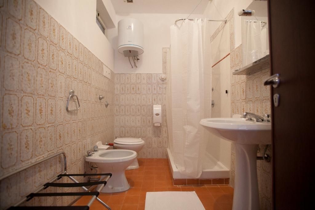 Uma casa de banho compacta com duas sanitas, uma pia, um chuveiro e um porta-toalhas.