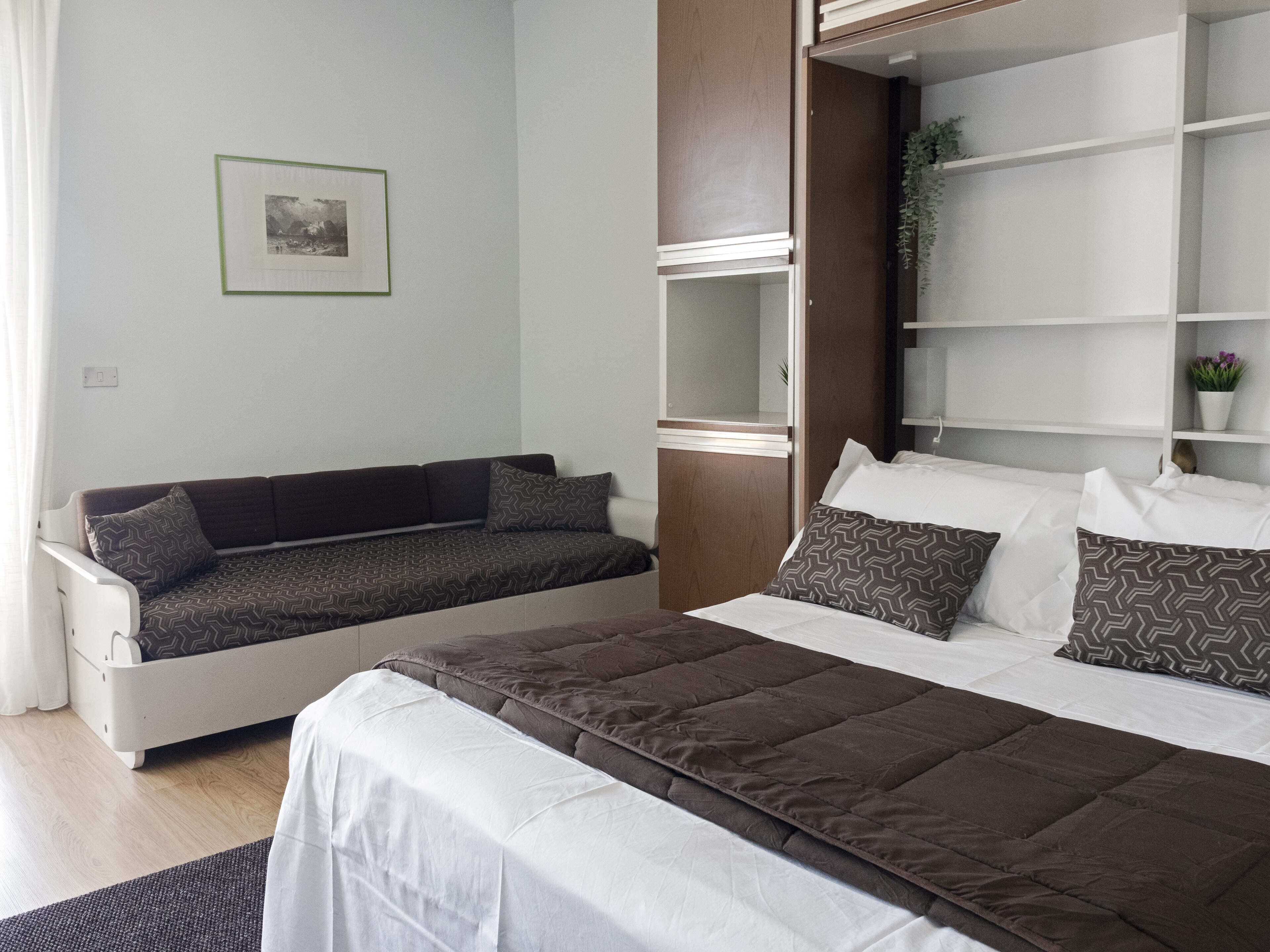 Een slaapkamer met een bed, een bank, een spiegel en een lijst met een foto aan de muur.