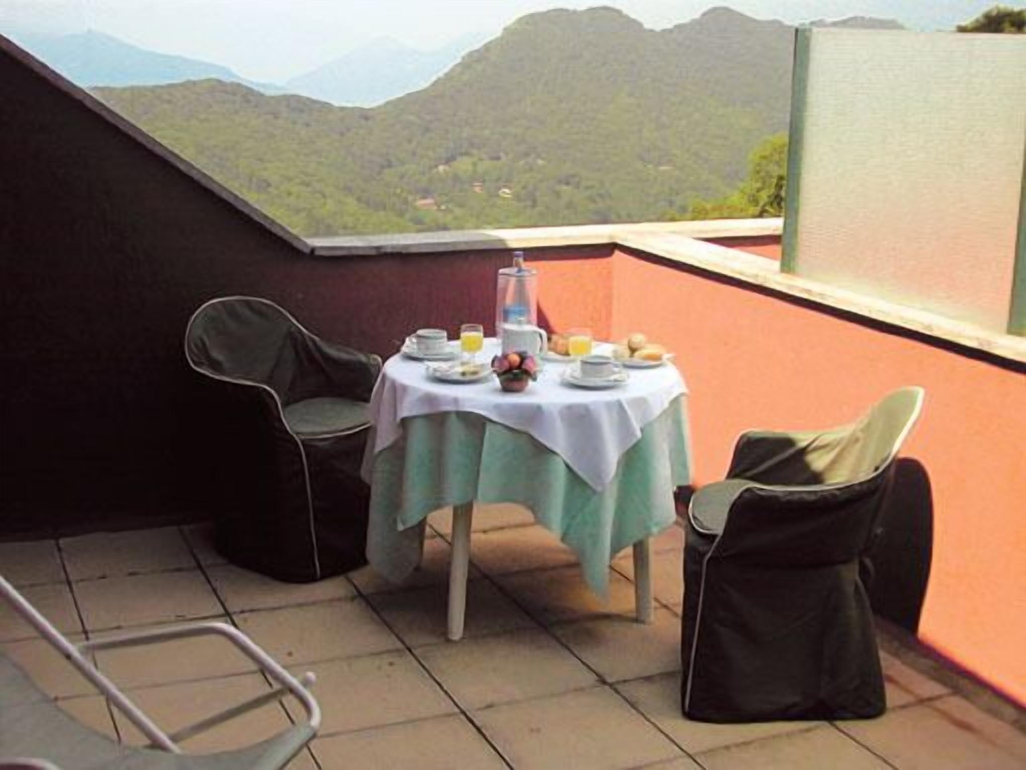A balcony with a table set for breakfast, overlooking a mountainous landscape.