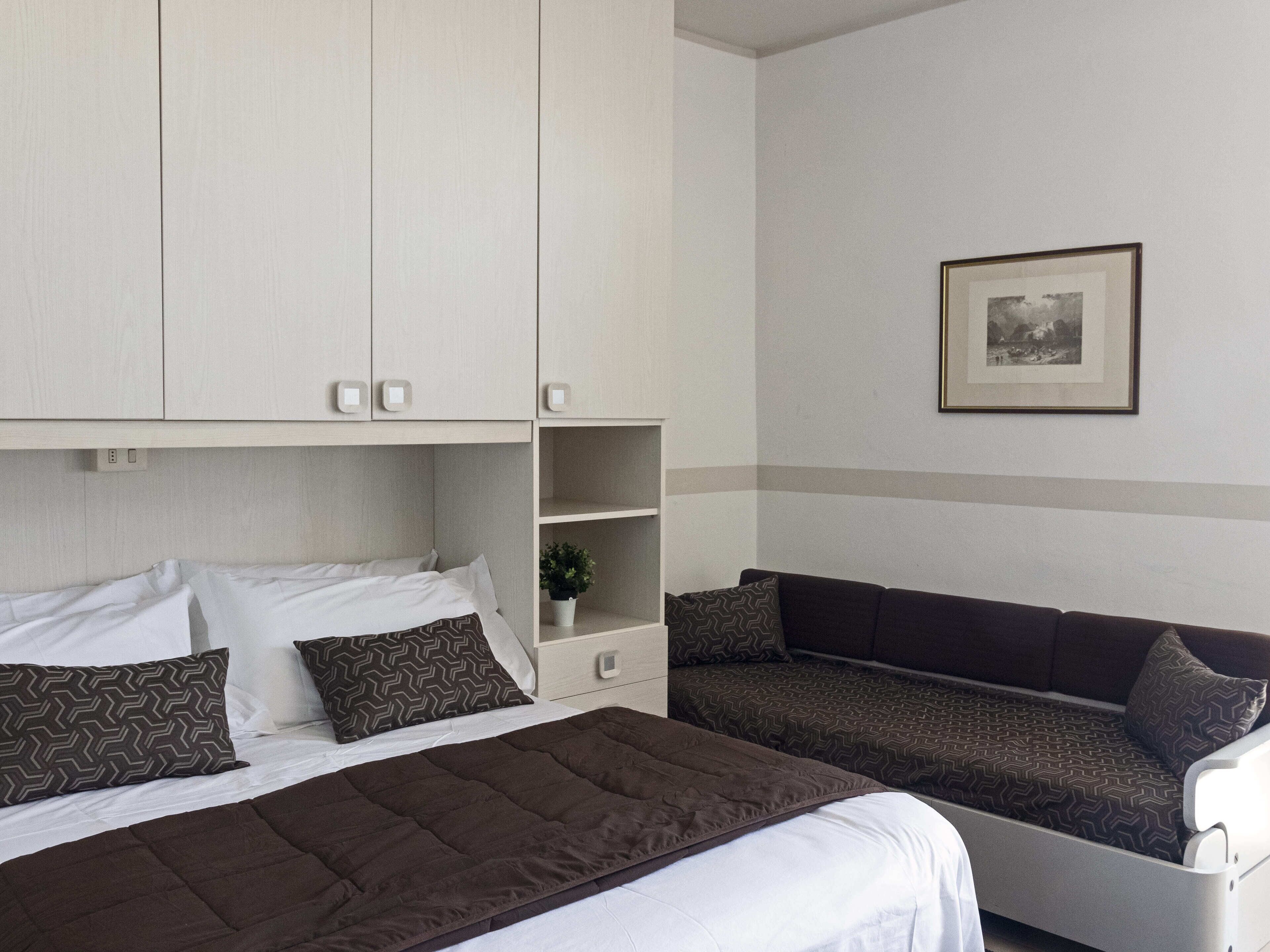 Ein Hotelzimmer mit Bett, einer Couch, einer kleinen Pflanze und einem gerahmten Bild an der Wand.
