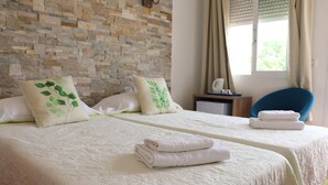 A hotel room with two beds, each with a white bedspread and green leaf-patterned pillows. There is a small table with a lamp and folded towels on it. - Hostal la Paloma II (Calpe)