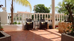 A patio area with two wicker tables and chairs, surrounded by potted plants and a white balustrade. - Hostal la Paloma II (Calpe)