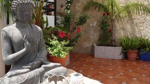 A statue of a seated figure in a courtyard with potted plants and a stone wall. - Hostal la Paloma II (Calpe)